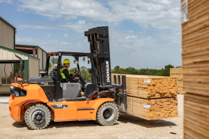 "Hoover team member operating an orange Doosan forklift, transporting a stacked load of lumber.